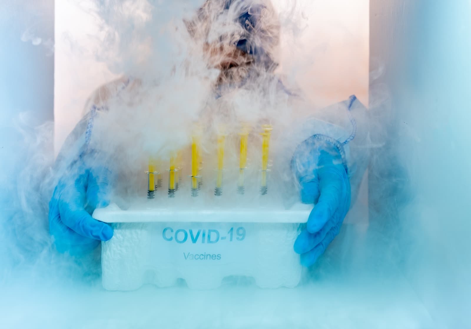 Gloved pharmacy technician handling a tray of vials in cold vapor, representing temperature-controlled handling of compounded sterile preparations before transport