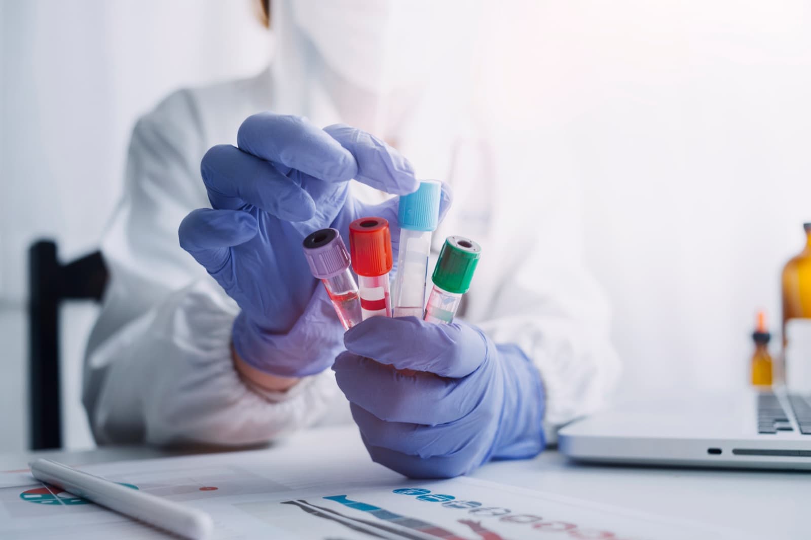 Gloved hands handling a labeled specimen in a clinical setting, representing time-critical newborn screening blood spot collection and transport